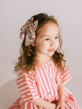 Load image into Gallery viewer, Young girl wearing a red and white striped dress with a floral headband against a plain background