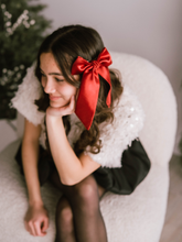 Load image into Gallery viewer, Woman sitting on a white chair with a red bow in her hair, surrounded by Christmas decorations.