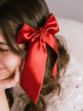 Load image into Gallery viewer, Person with a large red bow in their hair, blurred background