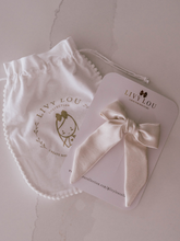 Load image into Gallery viewer, Baby headband with bow on a card and branded drawstring bag on a light background