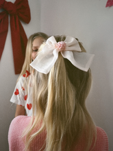 Load image into Gallery viewer, Person with a large white bow in their hair, wearing a white shirt with red hearts.
