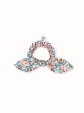 Load image into Gallery viewer, A fabric hair scrunchie with a bow design, featuring a delicate floral print in shades of blue, red, green, and pink on a white background.