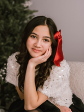 Load image into Gallery viewer, Woman with a red ribbon in her hair, sitting in front of a Christmas tree.
