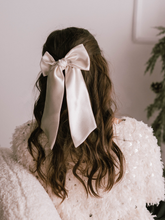 Load image into Gallery viewer, Person with long hair wearing a large white bow, wearing a white textured garment.
